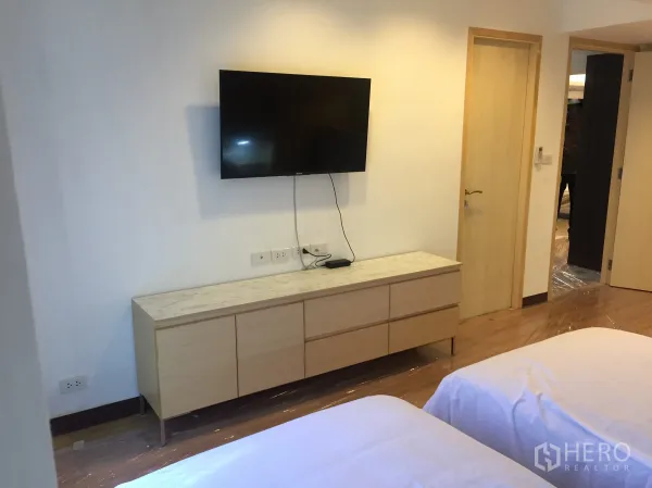 Condominium for rent in Pathum Wan, Bangkok - Secondary bedroom with twin beds, wall-mounted TV and light wood storage cabinet.