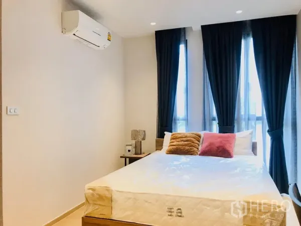 Condominium for rent or sale in Watthana, Bangkok - Bright bedroom with queen bed, tall windows, blackout curtains and wall-mounted air conditioner.