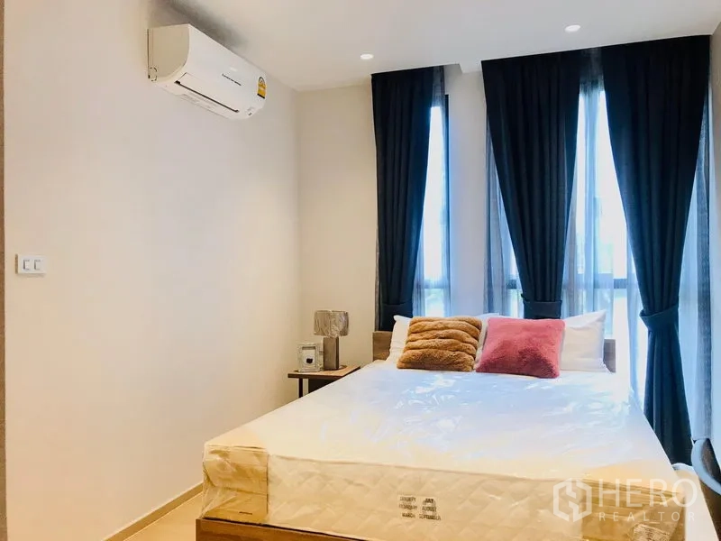 Condominium for rent or sale in Watthana, Bangkok - Bright bedroom with queen bed, tall windows, blackout curtains and wall-mounted air conditioner.