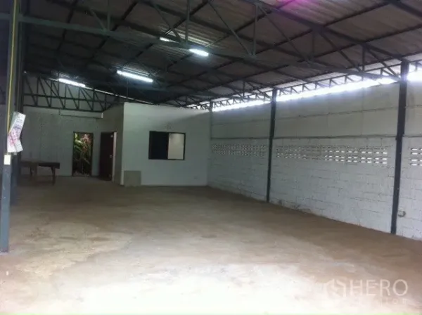 Warehouse for rent in Lam Luk Ka, Pathum Thani - Open-plan warehouse interior with high steel truss roof, block walls, bright lighting and a small office room.