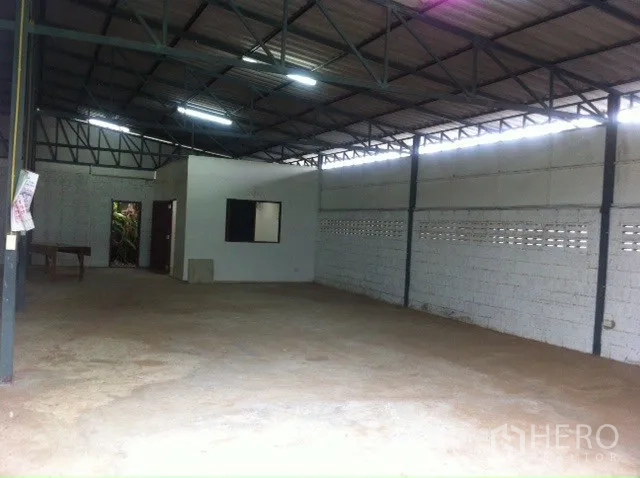 Warehouse for rent in Lam Luk Ka, Pathum Thani - Open-plan warehouse interior with high steel truss roof, block walls, bright lighting and a small office room.