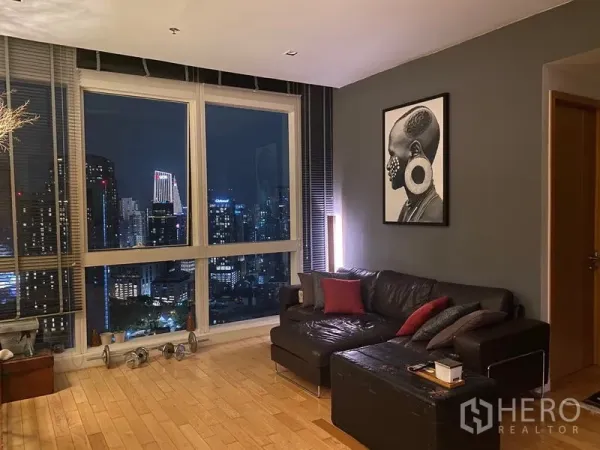 Condominium for rent in Khlong Toei, Bangkok - Seating area beside floor‑to‑ceiling windows offering dramatic night city views.