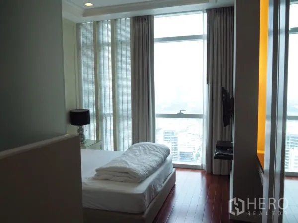 Condominium for rent in Pathum Wan, Bangkok - Master bedroom with wood flooring and panoramic floor‑to‑ceiling windows overlooking the city.