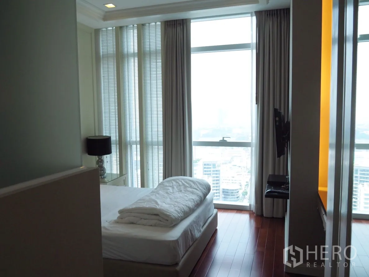 Condominium for rent in Pathum Wan, Bangkok - Master bedroom with wood flooring and panoramic floor‑to‑ceiling windows overlooking the city.