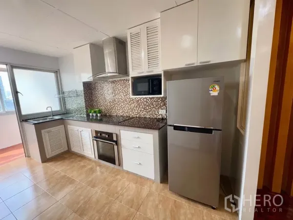 Condominium for rent in Huai Khwang, Bangkok - Modern kitchen with mosaic backsplash, granite countertop, stainless refrigerator, oven, cooktop and range hood beside a window.