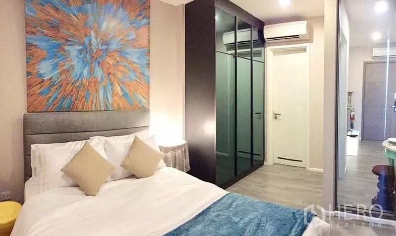 公寓 出租或出售在Watthana, Bangkok - 温馨卧室，软包床、大型镜面衣柜与抽象艺术装饰。