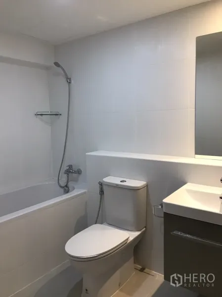 Condominium for rent in Watthana, Bangkok - Modern bathroom with bathtub and handheld shower, toilet with bidet spray, and a sleek vanity sink.