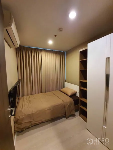 公寓 出租在Sathon, Bangkok - 紧凑卧室，单人床、壁挂电视、衣柜与开放格架，配遮光窗帘。