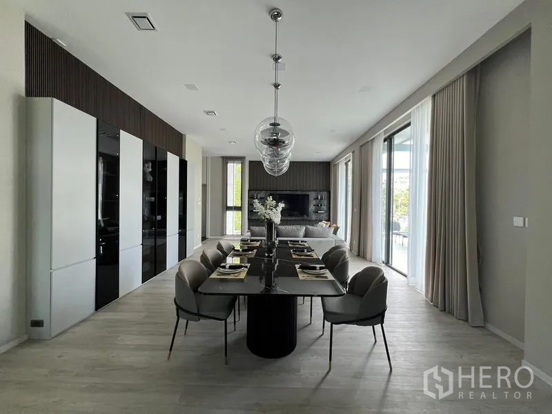 Detached House for rent in Saphan Sung, Bangkok - Dining room set for eight with trio pendant lights beside full-height windows.