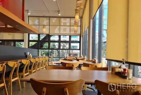 零售空间 出租在Watthana, Bangkok - 明亮的餐饮式室内空间，木质桌椅，落地玻璃与卷帘，吊灯和长吧台。
