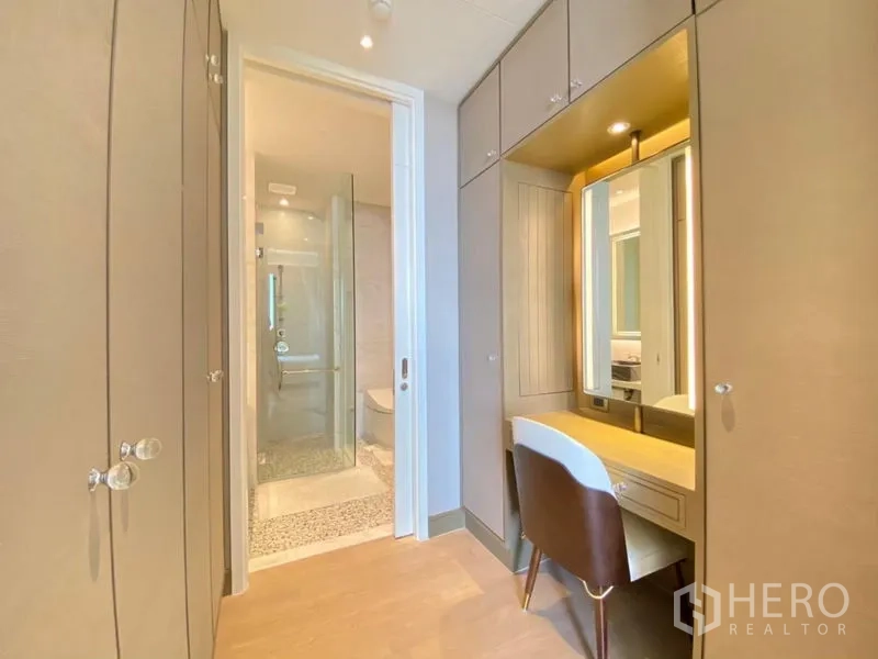 Condominium for rent in Khlong San, Bangkok - Dressing area with built‑in wardrobes, a lighted vanity, and direct access to a glass shower room.