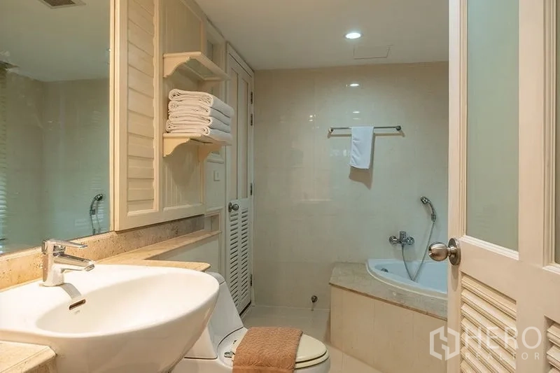 Apartment for rent in Bang Rak, Bangkok - Bathroom with round basin, mirrored cabinet, toilet and corner bathtub.