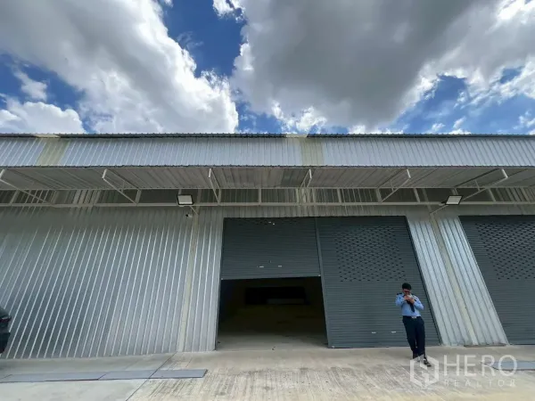 货栈 出租在Min Buri, Bangkok - 园区内金属板外立面仓库，双灰色卷帘门与雨棚装卸区