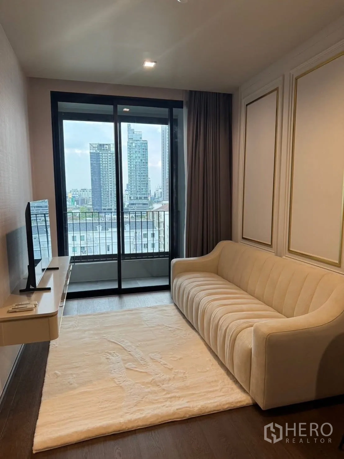 คอนโด for rent in Khlong Toei, Bangkok - ห้องนั่งเล่น โซฟาสีครีม พรม และวิวเมืองจากระเบียง
