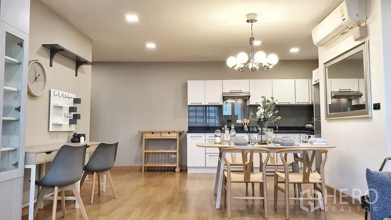 公寓 出租在Khlong Toei, Bangkok - 厨房与餐区，白色橱柜、玻璃门吊柜与木质餐桌，吊灯上方点缀。