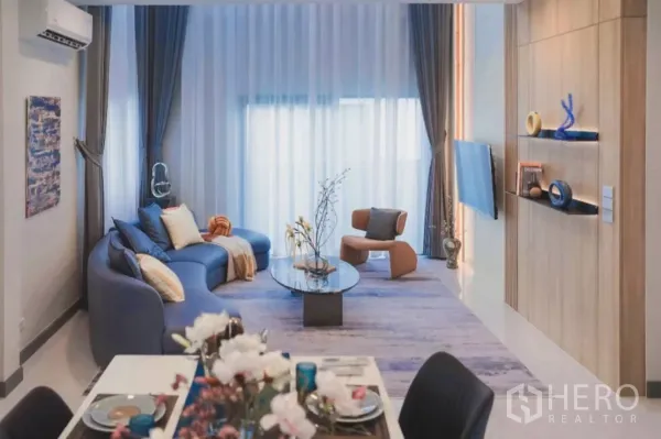 独立式住宅 出租在Bang Phli, Samut Prakan - 采光充足的客餐一体空间，落地窗、蓝色沙发与玻璃茶几。