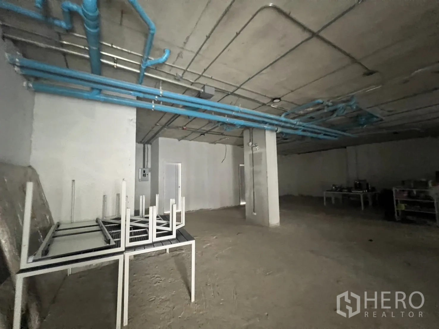 พื้นที่ขายปลีก ให้เช่า - พื้นที่ภายในแปลนเปิดโล่ง มีท่อสีน้ำเงินบนเพดานและโต๊ะวางซ้อน พร้อมปรับตกแต่ง