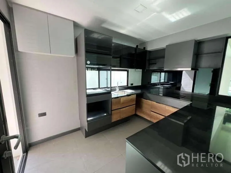 Detached House for rent or sale in Bang Phli, Samut Prakan - Modern U‑shaped kitchen with black countertops, wood drawers and stainless range hood.