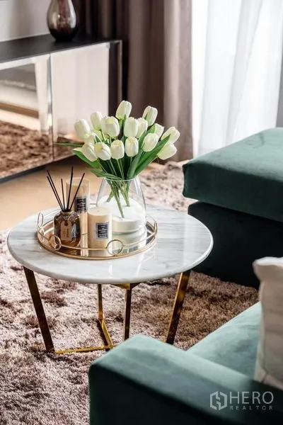 公寓 出租或出售在Bang Rak, Bangkok - 大理石茶几，白色郁金香与香薰蜡烛，旁为绿色沙发。