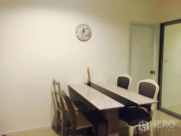 คอนโด ให้เช่าในKhlong Toei, Bangkok - มุมรับประทานอาหารสว่าง โต๊ะหินอ่อนกับเก้าอี้สี่ตัว ข้างประตูบานเลื่อนกระจกและนาฬิกาแขวนผนัง