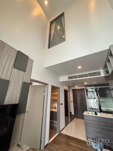 Condominium for rent or sale in Watthana, Bangkok - High-ceiling corridor with bathroom and bedroom doors beside a modern kitchenette.