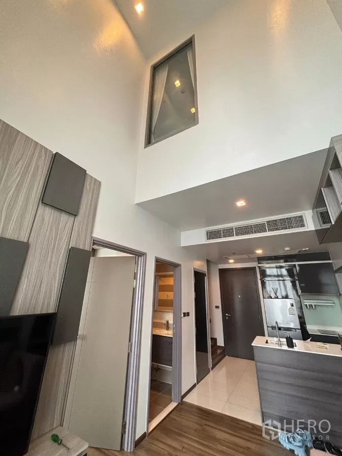 Condominium for rent or sale in Watthana, Bangkok - High-ceiling corridor with bathroom and bedroom doors beside a modern kitchenette.