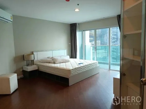 Condominium for rent or sale in Huai Khwang, Bangkok - Master bedroom with large windows, balcony access and wood flooring.