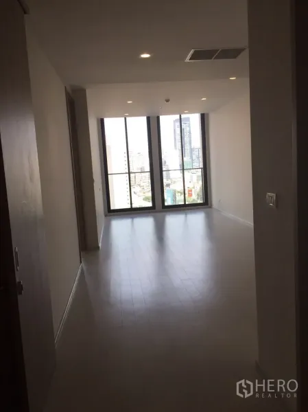 Condominium for sale in Pathum Wan, Bangkok - Open-plan living area with light wood floors leading to tall windows and city view.