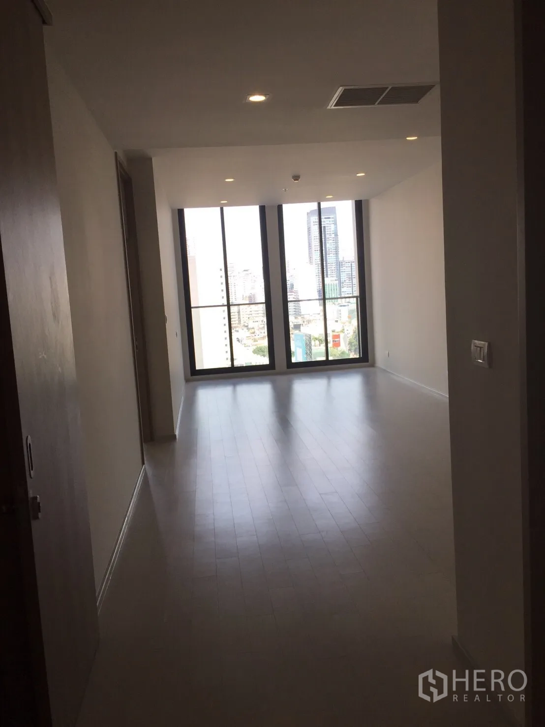 Condominium for sale in Pathum Wan, Bangkok - Open-plan living area with light wood floors leading to tall windows and city view.