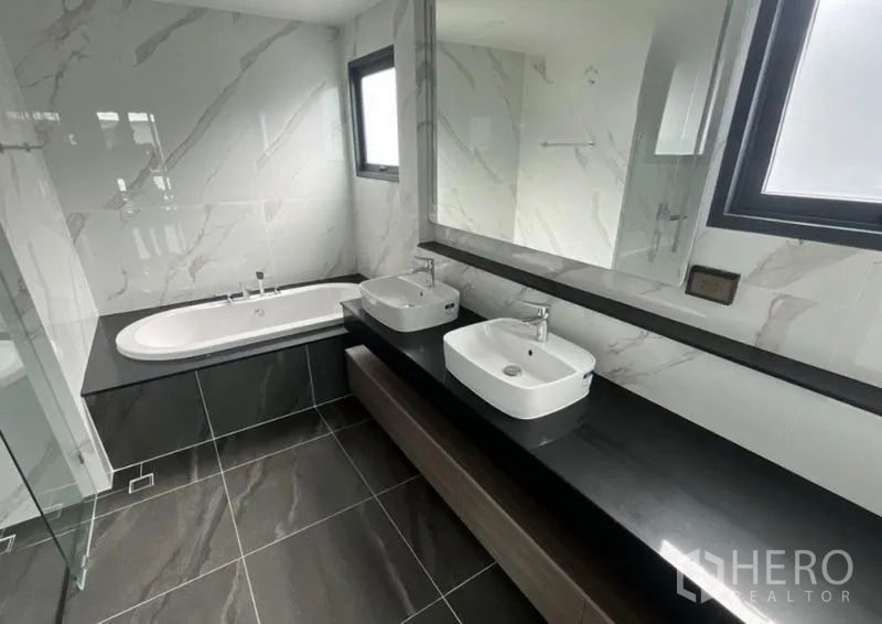 独立式住宅 出租在Bang Phli, Samut Prakan - 浴室设双台盆、大镜子、窗户与嵌入式浴缸。