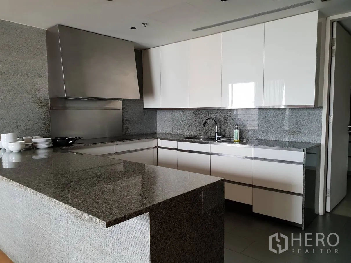 Condominium for rent in Sathon, Bangkok - Alternate view of the L-shaped kitchen showcasing granite countertops, white cabinetry and a stainless backsplash.
