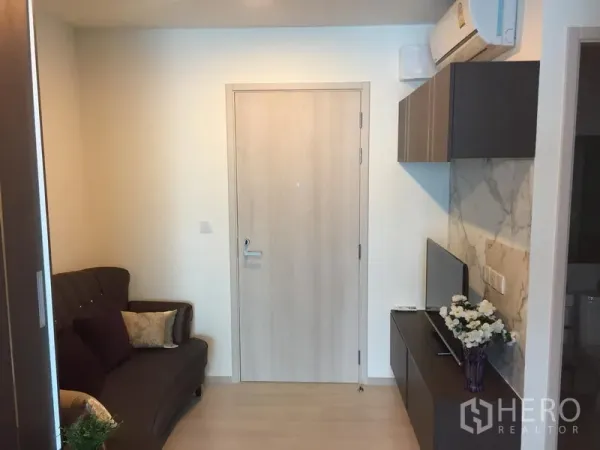 Condominium for rent in Huai Khwang, Bangkok - Compact living room with dark sofa, wall cabinets, TV console and marble accent wall under air conditioning.