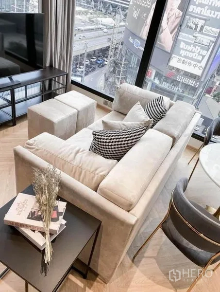 Condominium for rent in Din Daeng, Bangkok - Top-down view of sofa seating, side table with books and large urban views through glass walls.