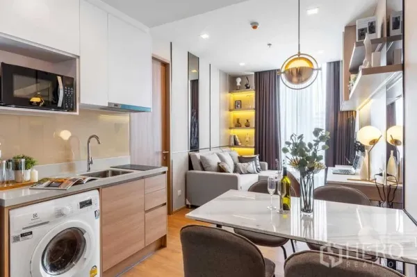 Condominium for rent in Watthana, Bangkok - Compact kitchen with washer, microwave and marble dining table facing a cozy living room.