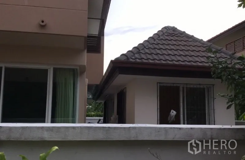 Detached House for rent in Bang Phli, Samut Prakan - Side yard view showing the main house and a small tiled-roof outbuilding behind a low wall.