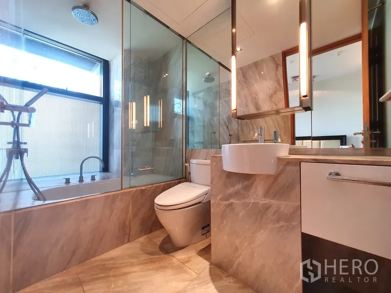 Condominium for rent in Sathon, Bangkok - Marble bathroom with glass shower enclosure and separate bathtub by the window.