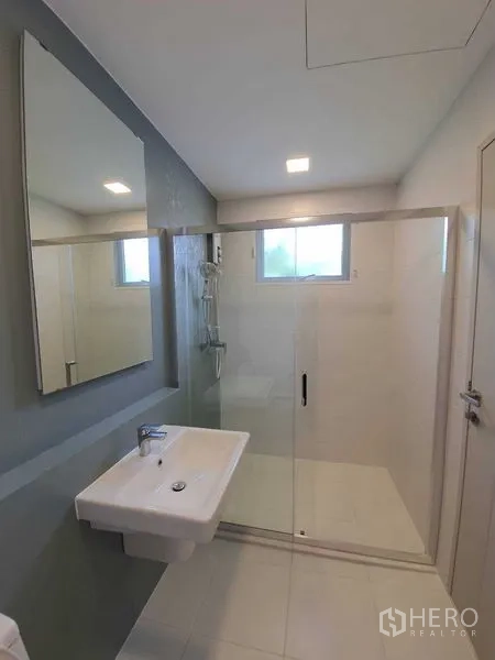Townhouse for rent - Modern bathroom with wide glass shower enclosure, vanity sink, and mirror.