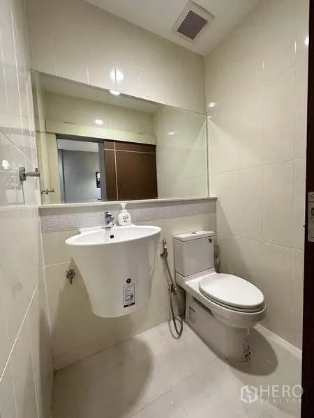 Townhouse for rent in Chom Thong, Bangkok - Guest bathroom with toilet, pedestal-style wall sink and wide mirror.