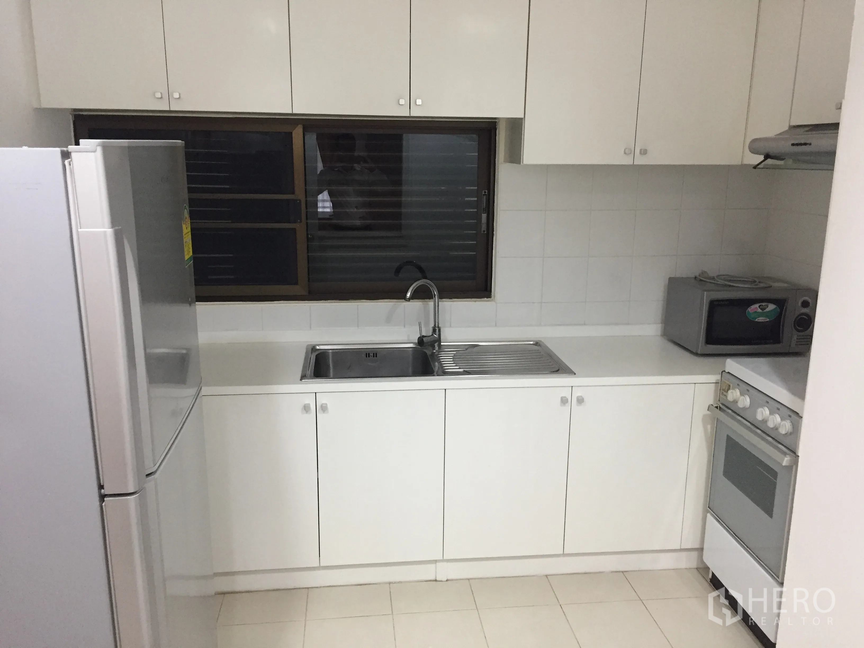 คอนโด ให้เช่าในWatthana, Bangkok - ห้องครัวแยกโทนขาวพร้อมตู้บิวท์อิน อ่างล้างจาน เตาอบ ไมโครเวฟ และตู้เย็นขนาดใหญ่ข้างหน้าต่างบานเกล็ด