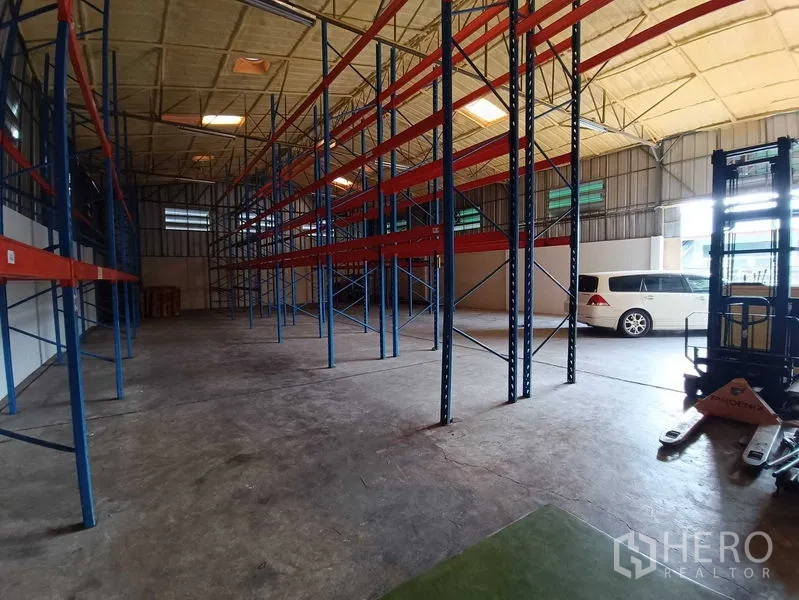 Warehouse for rent in Suan Luang, Bangkok - Wide-angle view of racked warehouse with reach truck and parked car.