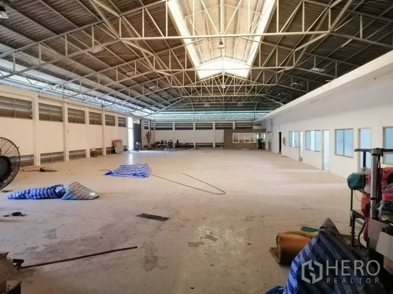 Factory for rent in Pathum Thani - Spacious production hall with high steel truss roof, skylight and attached office rooms with windows.