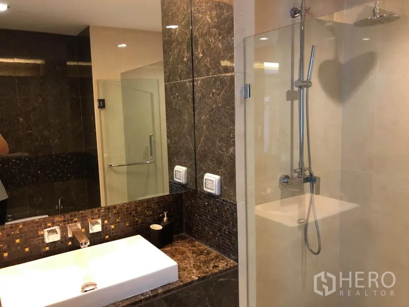 Condominium for rent in Watthana, Bangkok - Modern bathroom with marble vanity, large mirror and a glass-enclosed rain shower.