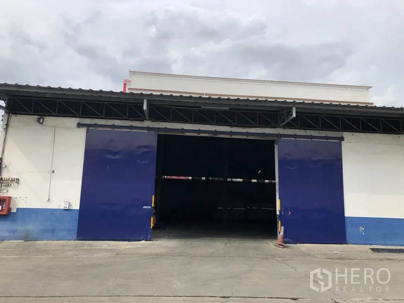 Warehouse for rent in Samut Prakan - Front facade of the warehouse with extra-wide blue sliding doors open to the loading bay.