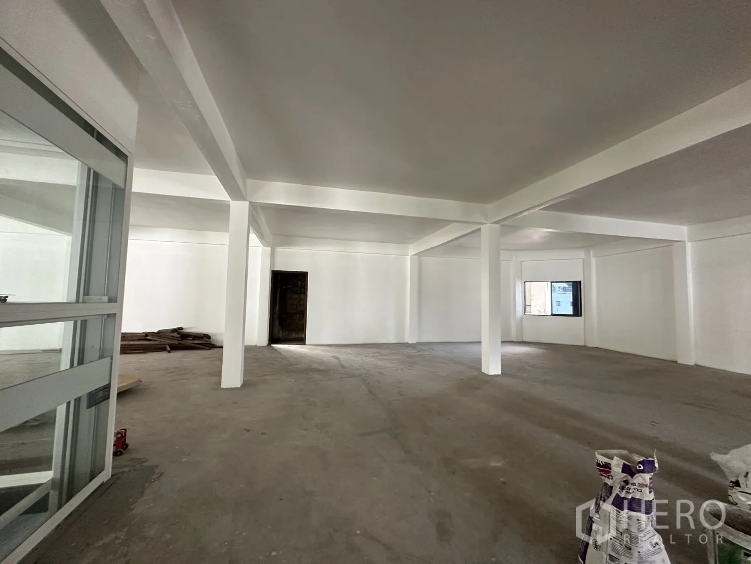 零售空间 for rent in Watthana, Bangkok - 宽阔的白色零售大厅，设多根立柱、窗户与门口，适合二次装修。