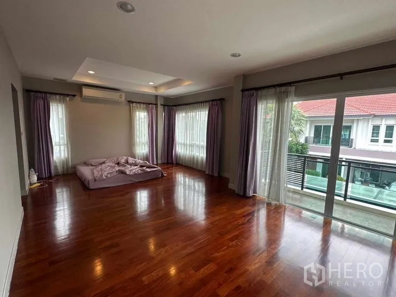 Detached House for sale in Saphan Sung, Bangkok - Large master bedroom with hardwood floors, balcony access and curtain-lined windows.