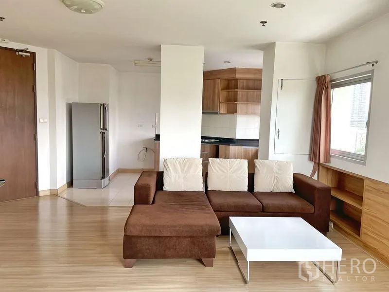 คอนโด ให้เช่าในKhlong Toei, Bangkok - มุมนั่งเล่นพร้อมโซฟารูปตัวแอล โต๊ะกลางสีขาว มองไปยังครัวแบบเปิด