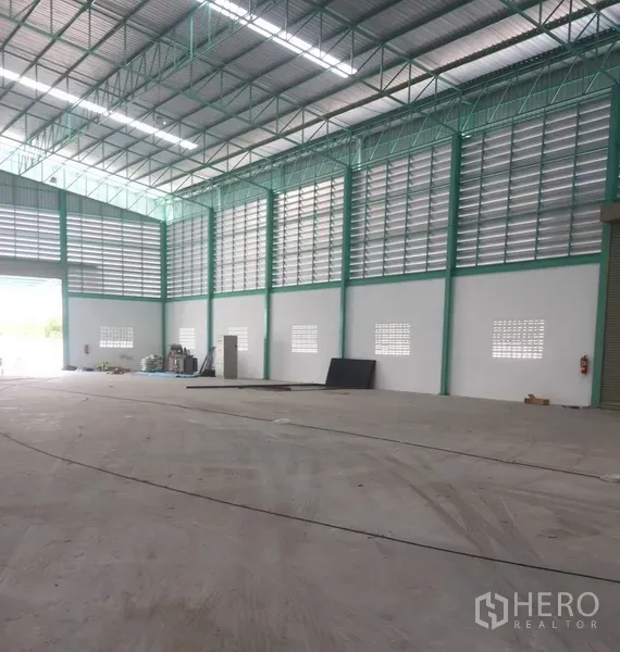 Warehouse for rent in Samut Prakan - Corner view of modern warehouse showing tall walls, service doors, ventilation panels, and an open loading area.