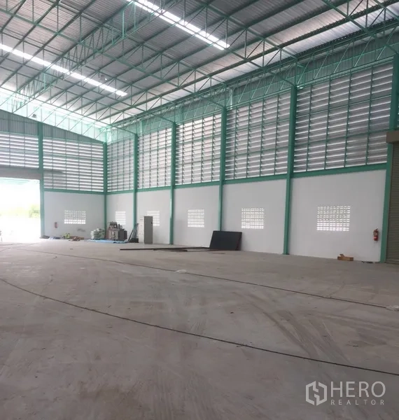 Warehouse for rent in Samut Prakan - Corner view of modern warehouse showing tall walls, service doors, ventilation panels, and an open loading area.