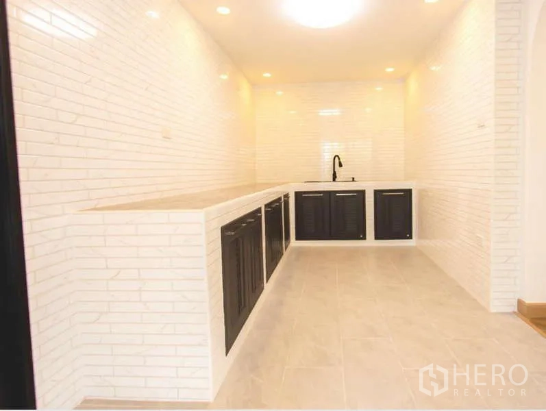 Detached House for sale in Wang Thonglang, Bangkok - Long galley kitchen finished with white brick-style tiles, black cabinets and recessed lighting.