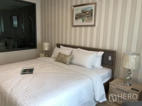 Condominium for rent in Watthana, Bangkok - Cozy bedroom with striped wallpaper, white linens, bedside lamps, and a window to the en-suite bathroom.